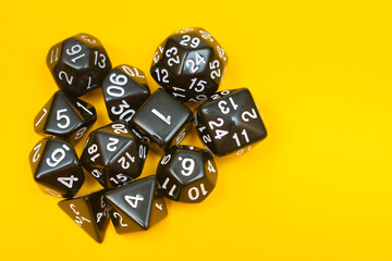 Group of black dice D20, D10, D12, D8, D6 on a trendy yellow background: space for text, top view, concept of role-playing games and games for the whole family at home