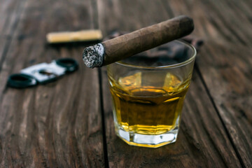 Contrast photo of a smoldering cigar lying on a glass of whiskey on a wooden table