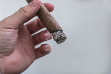 A man's hand holds a lighted smoldering cigar on a light background