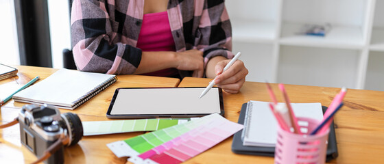 Female designer student doing assignment on digital tablet and designer supplies