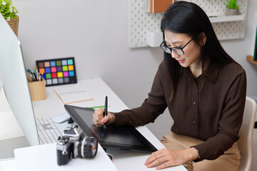 Female designer working with drawing tablet on computer desk in office room