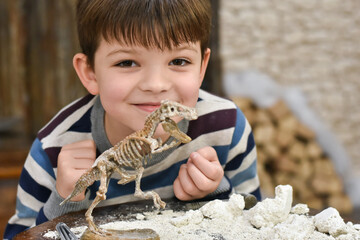 Happy child digging the dinosaur and having fun with archaeology excavation kit. Boy plays an...