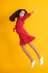Cute charming dreamy teenage girl in red dress with floral print, lies on yellow studio background. Caucasian brunette jumping on background colored wall.Copy space