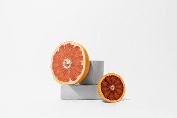 Half of grapefruit and orange on gray cube and parallelepiped pedestals, white background, copy space. Citrus fruits on geometric podium mockup for product. Minimalism abstract composition
