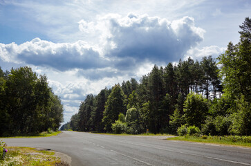 Fototapeta na wymiar Road with green trees against cloudy blue sky