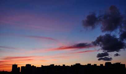Colorful dramatic sky with clouds at sunset. City during warm sunset