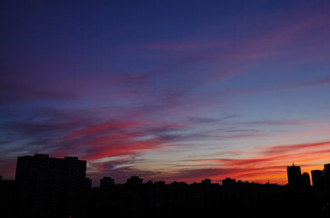 Colorful dramatic sky with clouds at sunset. City during warm sunset