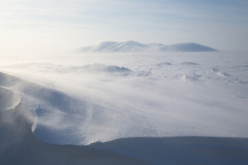 Winter Arctic landscape. View of the snow-covered tundra and snow-covered mountains. Very cold and windy weather. Blowing blizzard. Chukotka, Siberia, Russia. Low depth of field, blurred background. © Andrei Stepanov