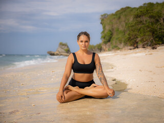 Fototapeta na wymiar Lotus pose. Beautiful woman sitting on the sand in Padmasana. Yoga and meditation concept. Healthy lifestyle. Yoga retreat. Thomas beach, Bali