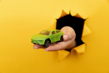 Female hand with house car through a rip in yellow paper wall close-up. Sale and rent concept