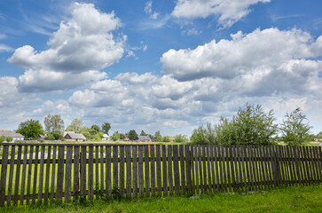 Obraz premium Old wooden fence against a blue sky with clouds on a sunny day. Background of old wood planks rustic on farm