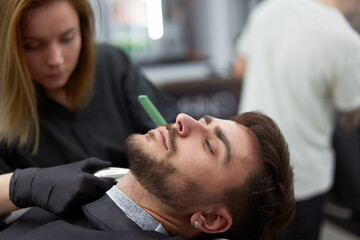 Young beautiful caucasian woman hairdresser cuts beard  handsome man at modern barbershop