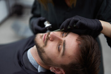 Young beautiful caucasian woman hairdresser cuts beard  handsome man at modern barbershop