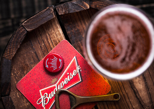 LONDON, UK - APRIL 27, 2018: Original glass of budweiser beer with beer coater and bottle opener on wooden barrel.