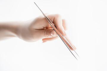 Close-up hand of master holds tools for eyebrow correction and eyelash extension tweezers and tongs...