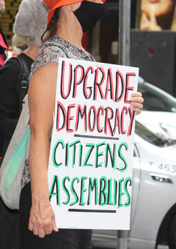 Extinction Rebellion Sydney Parade - "Still Climate Emergency" A woman wearing a face mask holding a sign reading "upgrade democracy - citizens assemblies".