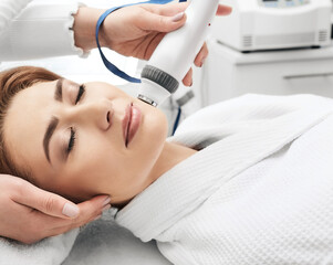 Adult woman during rf-lifting face skin tightening with her beautician at a beauty salon, close-up