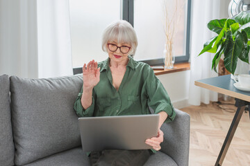 senior woman talking with family by video call from home. Work with lap top. Lockdown, family,...