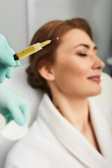 Naklejka premium Syringe with a patient's blood plasma in a cosmetologist's hand for a plasmolifting of a woman's facial skin. Plasma therapy, skin cell restoration