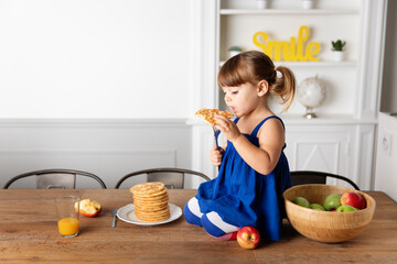 Little girl kneeling on kitchen table eating pancake