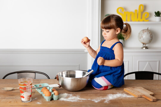 Toddler girl sitting on kitchen table holding an egg