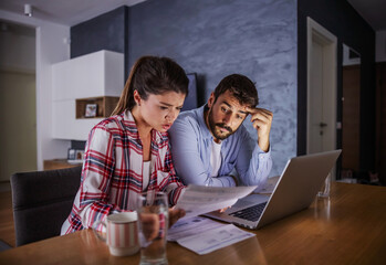 Nervous young couple sitting at home, paying bills online.