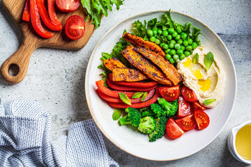 Vegan salad bowl with sweet potatoes, broccoli, tomato, peas and hummus. Cooking healthy food concept.
