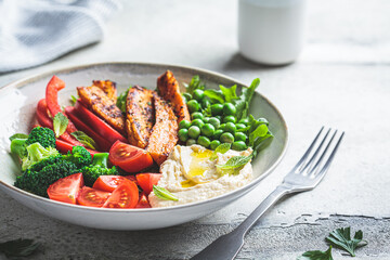 Vegan salad bowl with sweet potatoes, broccoli, tomato, peas and hummus.