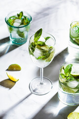 Mojito cocktail with mint and lime in glasses, white marble background. Refreshing drink with lime and mint in glasses.