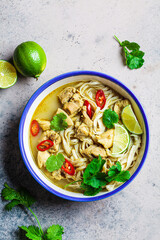 Thai green curry noodles with chicken, chili and cilantro in white bowl.