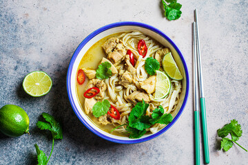 Thai green curry noodles with chicken, chili and cilantro in white bowl.