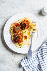Spaghetti pasta with meatballs in tomato sauce and herbs on white plate, top view. Comfort food concept.