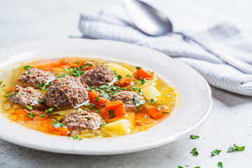 Homemade meatballs soup with vegetables in white plate, gray background. Comfort food concept.