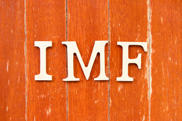 Alphabet letter in word IMF (abbreviation of International Monetary Fund) on old red color wood plate background