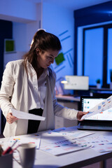 Busy business woman looking on financial reports, checking statistics graphs standing at desk late...