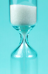 Sand clock on turquoise background. Hourglass as time passing concept. Close up photo.