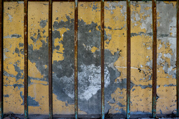 rusty metal bars from a prison or jail over an old yellow wall of cement in the background with peeling painting