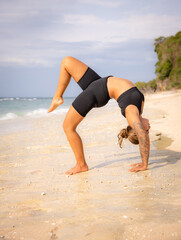 Beach yoga. Young woman practicing Eka Pada Chakrasana, One Legged Wheel Pose. Upward facing bow pose is a deep backbend. Flexibility, strength, patience. Yoga retreat. Thomas beach, Bali
