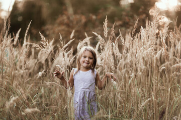 Free emotional caucasian girl child in summer running in tall grass, concept of freedom, childhood and emotions, happy childhood in nature