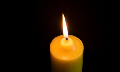 One candle is lit in the dark or on a black background.