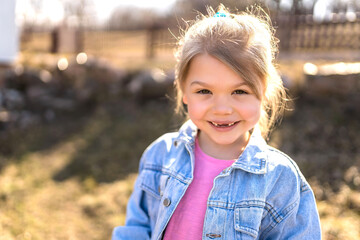 A seven year old girl laughs and rejoices in the spring on the street in a denim jacket.
