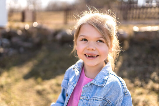 A seven year old girl laughs and rejoices in the spring on the street in a denim jacket.