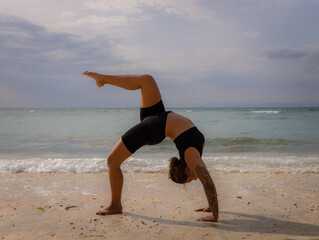 Outdoor yoga. Young woman practicing Eka Pada Chakrasana, One Legged Wheel Pose. Upward facing bow pose is a deep backbend. Flexible, strong body. Yoga retreat. Thomas beach, Bali