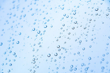 Fototapeta na wymiar Close-up of raindrops or snow drops on a blue windowpane. Freshness background and texture of drops on the surface