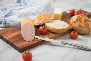 Feine Kalbsleberwurst auf Weizen Rosen Brötchen dazu Tomaten, Butter und Messer mit Holzbrett,...