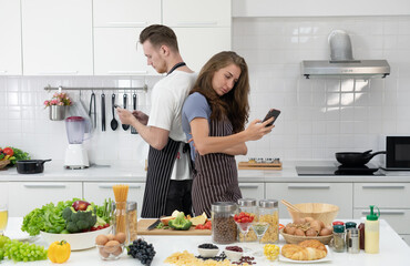 young caucasian couple using smartphone while cooking healthy food for breakfast. togetherness concept