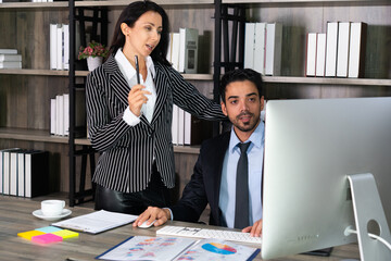 young middle east businessman sitting on chair and caucasian businesswoman standing beside her colleague in office. business concept