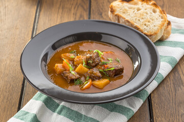 beef stew with bread toast in grey plate on wooden table