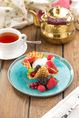 ice cream in waffle cone with fresh berries and cup of tea on wooden table