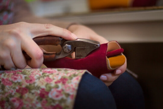 Manos de mujer fabricando, de manera artesanal, un zapato utilizando herramientas de zapatero. Colocando la tela en una horma.